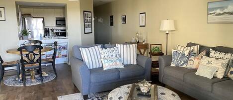 A living room with a grey sofa, a coffee table, and a dining area with a wooden table and chairs.