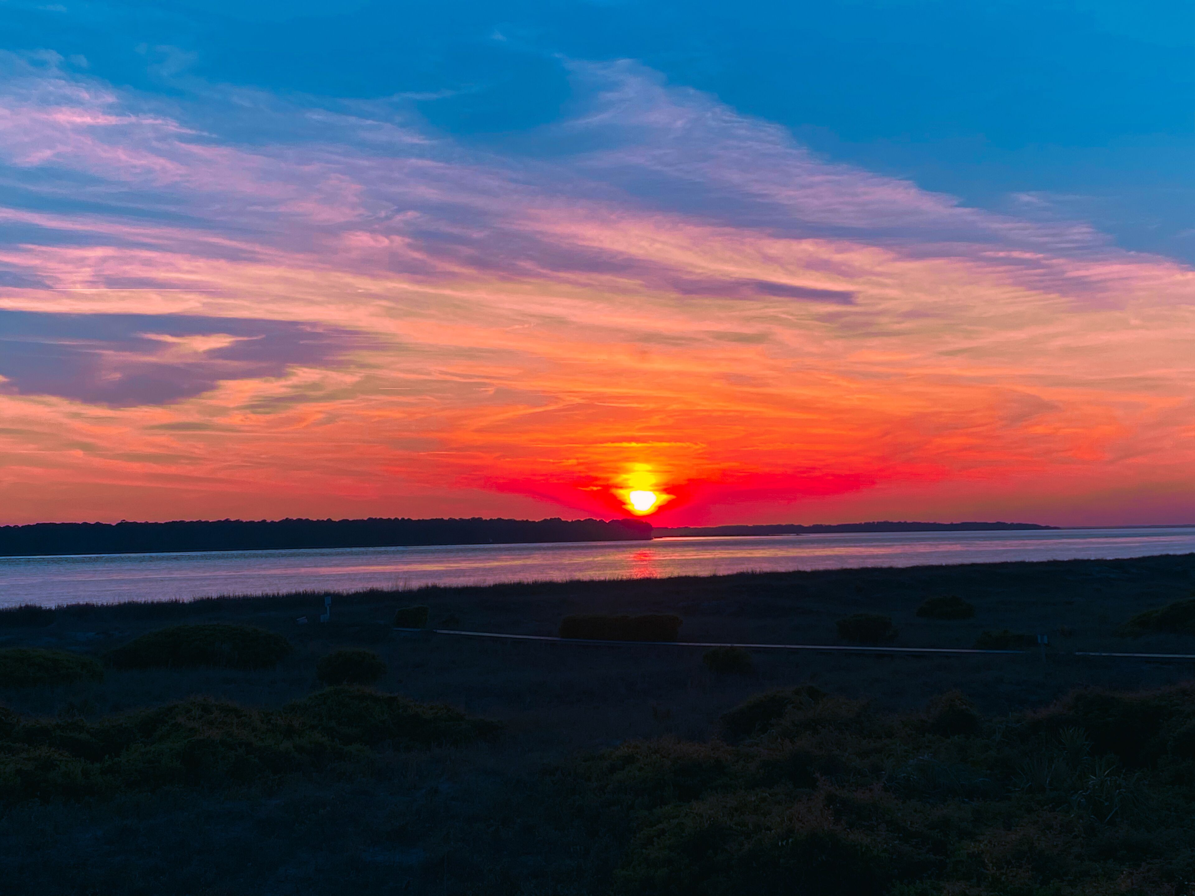 A sunset over a body of water with a silhouette of land in the distance.