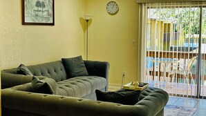 Ein Wohnzimmer mit einer Couch, einer Uhr und Blick auf eine Terrasse.