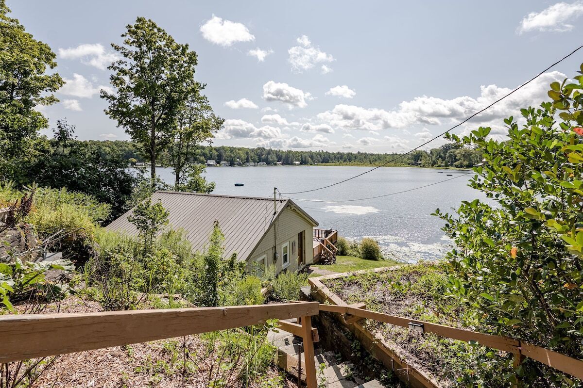 Une propriété au bord du lac, dotée d’une terrasse en bois, d’une maison avec un toit en métal et offrant une vue sur le lac.