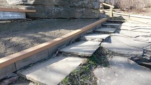 Un escalier en pierre mène à une terrasse en bois, à côté d’une grande formation rocheuse.