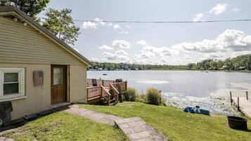 Uma casa com um deck com vista para um lago, um caminho que leva à porta e um pequeno barco atracado perto da água.