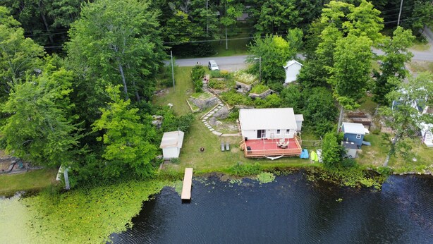 Une maison avec une terrasse rouge, un petit porche et une jetée qui s’avance sur un lac entouré d’une forêt dense.