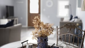 Un coin repas avec une table dressée pour deux personnes, un vase contenant des fleurs séchées et une chaise dotée d’un repose-tête en métal.