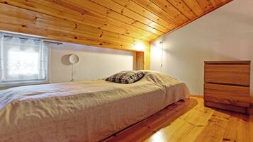 A bedroom with a wooden ceiling, a bed with a plaid pillow, a bedside table, and a dresser.