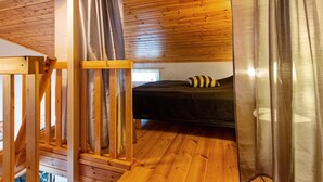 A wooden cabin interior with a bed, curtains, and a wooden ceiling.