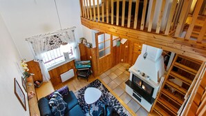 A cozy cabin interior with a wooden ceiling, a loft bedroom with a balcony, a living area with a sofa and a TV, and a fireplace.