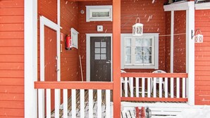A red wooden house with a white porch, a door, and a window.