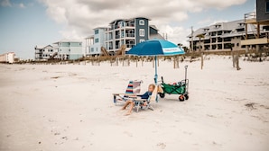 A beach scene with a person relaxing under a Nautica umbrella, a beach chair, and a beach cart. - Grand Balcony Views, Pool, Hot Tub (Mexico Beach)