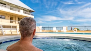 A man in a hot tub with a view of a pool and a building in the background. - Grand Balcony Views, Pool, Hot Tub (Mexico Beach)