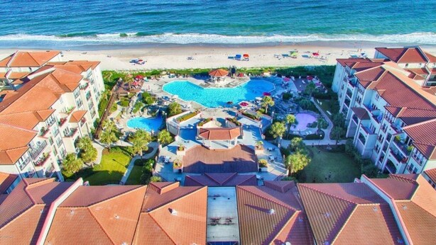 A resort with multiple buildings, a central swimming pool, and a beach area.