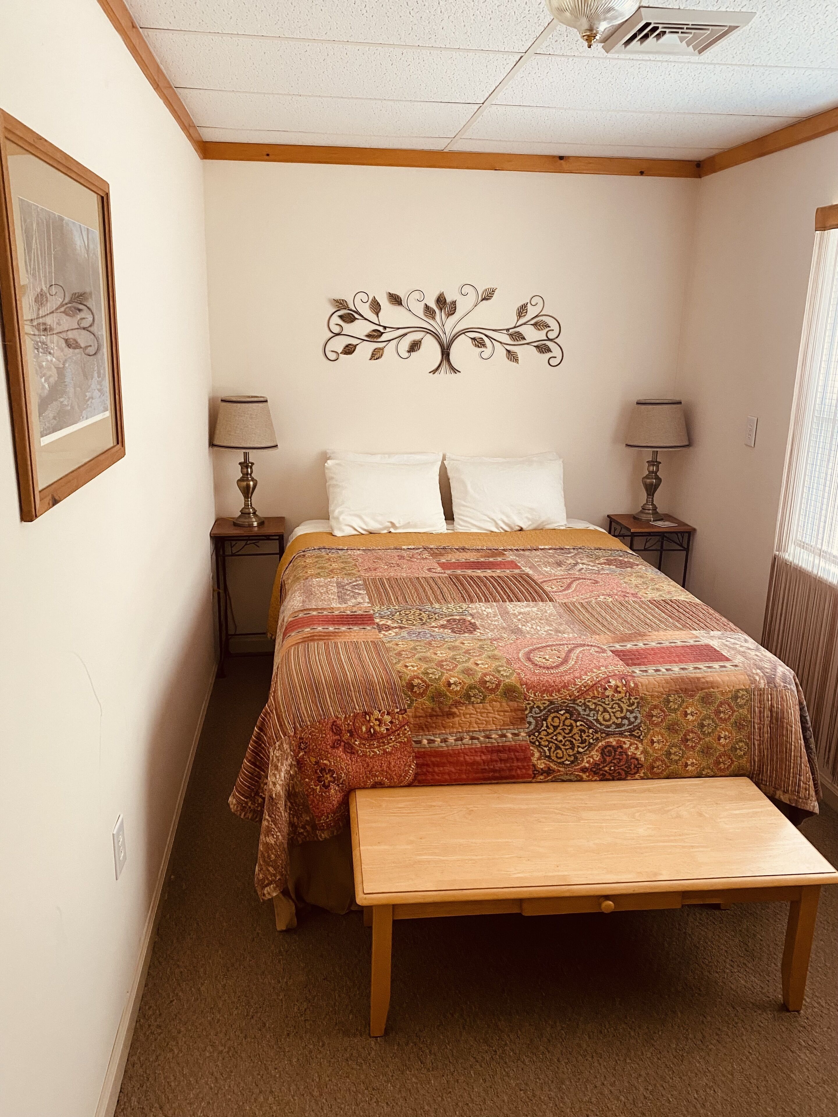 Ein Schlafzimmer mit einem Bett, zwei Nachttischen, einer Wandlampe, einer Bank, einem Deckenventilator und einem gerahmten Bild.