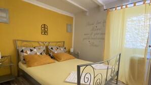 A bed with a metal frame, a yellow bedspread, and two pillows. There is a wall with a decorative item and a quote. - Apartment in center Old town (Dubrovnik)