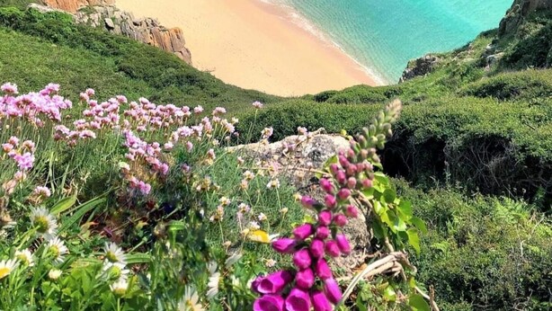 Eine Küstenlandschaft mit Sandstrand, Felsküste und klarem türkisblauem Wasser.