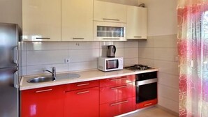 Ett kök med vita överskåp, ett rött underskåp, en diskho i rostfritt stål, en mikrovågsugn, en gasspis och en vattenkokare.