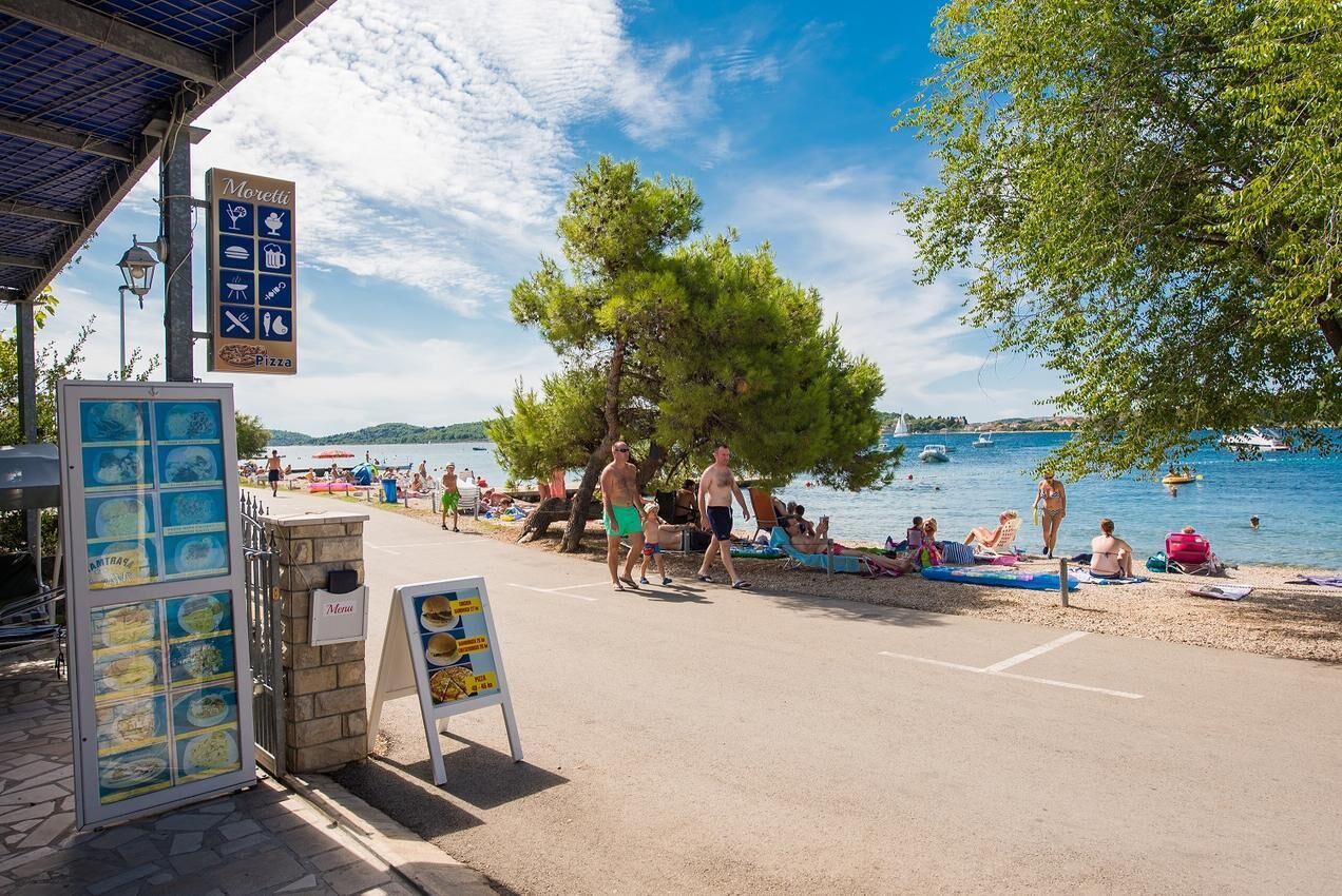 A seaside restaurant with outdoor seating, a menu board, and a view of the beach and water.