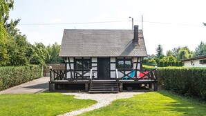 Een traditioneel vakwerkhuis met schuin dak, een houten veranda en een grindpad dat naar de ingang leidt.