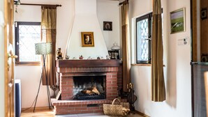 Een gezellige woonkamer met een schouw van baksteen, houten balken en een groot raam met gordijnen.