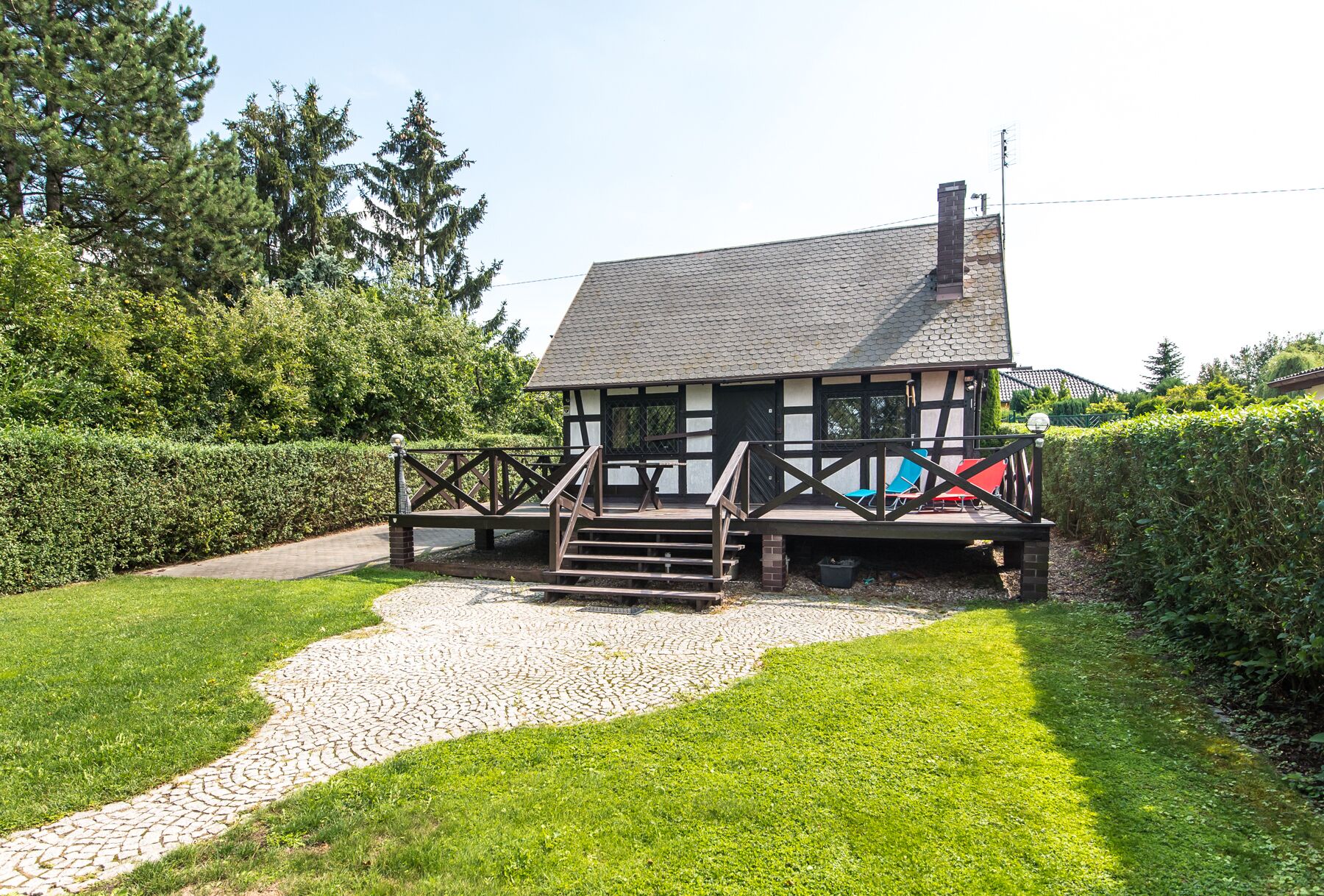 Ein traditionelles Fachwerkhäuschen mit einem Stehendach, einer Holzterrasse und einem Kiesweg, der zum Eingang führt.