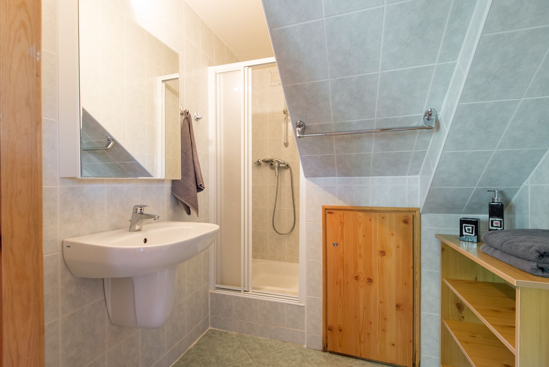 A bathroom with a sink, mirror, shower, and wooden door.