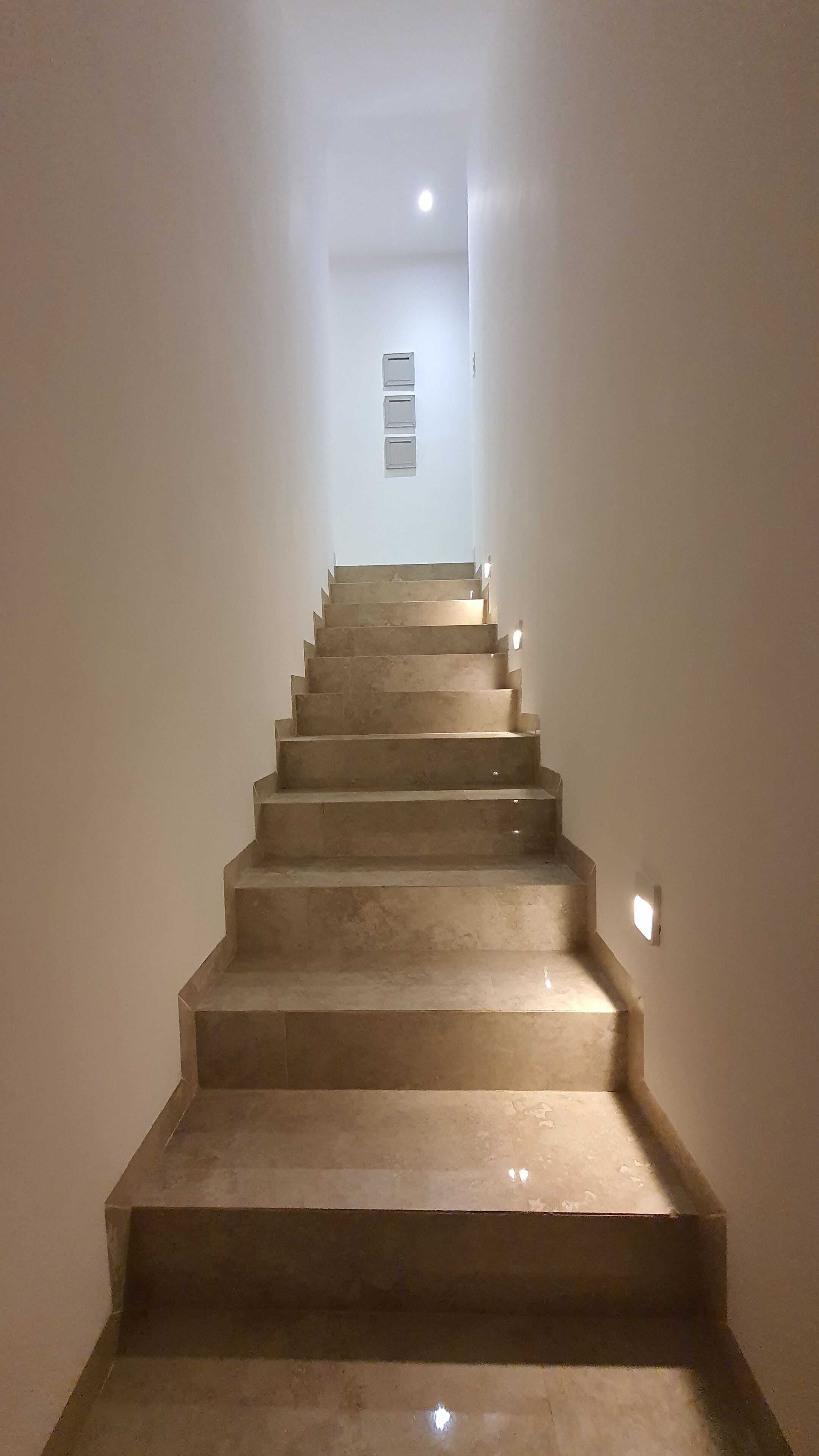 Uma escada com corrimão, que leva a um patamar com um lustre.
