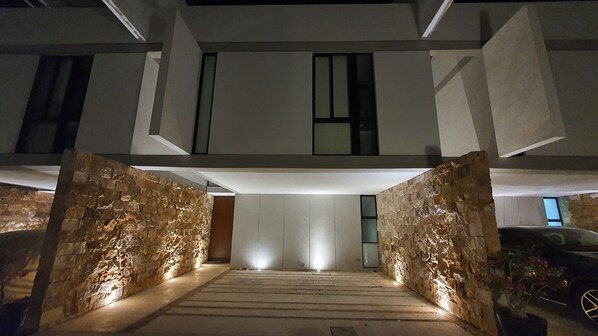 A modern building entrance with a stone facade, a staircase leading to a second floor, and a car parked outside.