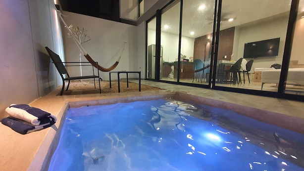 A modern outdoor pool area with a glass enclosure, a hammock, and a seating area with chairs. - Casa BJ37 Mérida Norte, la mejor ubicación. (Mérida)