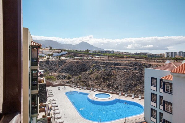 A swimming pool with lounge chairs, a mountainous backdrop, and a clear sky.
