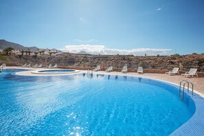 A swimming pool with sun loungers and a view of mountains.