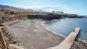 Une plage côtière avec un rivage rocheux, une promenade en béton et des bâtiments en arrière-plan.