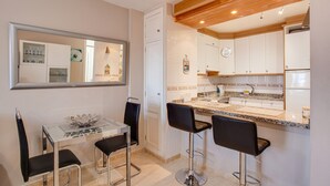 Une cuisine de taille réduite avec des meubles blancs, un plan de travail en granit et un plafond en bois.