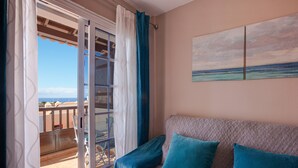 Un balcon avec vue sur la mer, un canapé agrémenté de coussins turquoise et un tableau accroché au mur.