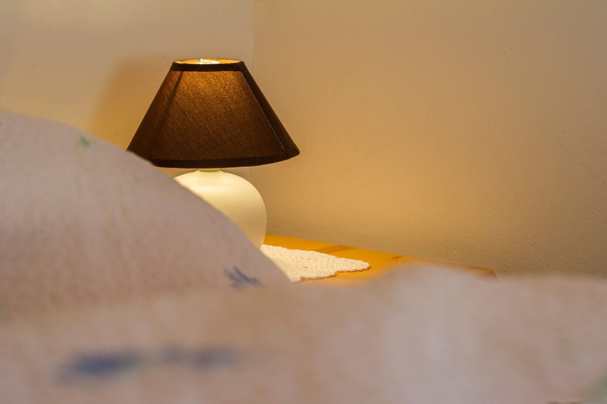 A bedside lamp on a wooden nightstand with a white lampshade.