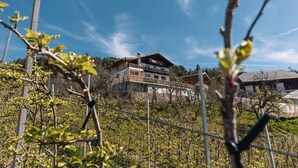 A multi-story house with a balcony, surrounded by a fence and trees. - Apartment "Malgorerhof Lavendel" with Mountain View, Wi-Fi, Balcony & Shared Garden (Jenesien)