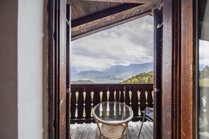 An open wooden door leading to a balcony with a wicker chair and a glass table, overlooking a mountainous landscape. - Apartment "Malgorerhof Lavendel" with Mountain View, Wi-Fi, Balcony & Shared Garden (Jenesien)