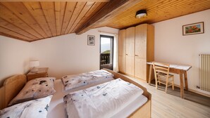 A bedroom with two beds, a wooden desk, a chair, a radiator, and a door leading to a balcony. - Apartment "Malgorerhof Lavendel" with Mountain View, Wi-Fi, Balcony & Shared Garden (Jenesien)