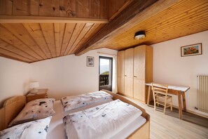 A bedroom with two beds, a wooden desk, a chair, a radiator, and a door leading to a balcony.