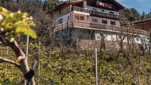 Ein großes, zweistöckiges Gebäude mit mehreren Balkonen, umgeben von Bäumen und blauem Himmel.