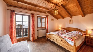 Ein schlicht eingerichtetes Schlafzimmer mit Holzbett, Fenster mit Vorhängen, Heizkörper und Nachttisch mit Lampe.