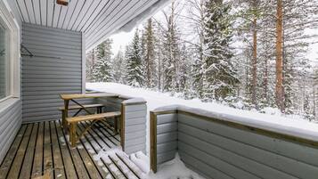 Une terrasse en bois avec un banc et une table, entourée d’arbres couverts de neige.