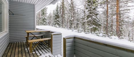 Eine Holzterrasse mit einer Bank und einem Tisch, umgeben von schneebedeckten Bäumen.