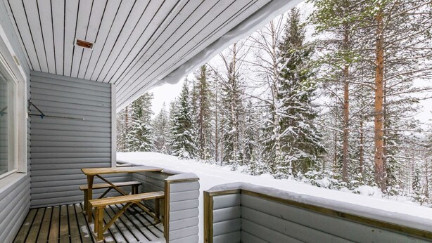 Katettu puinen terassi, jossa on pöytä ja penkkejä, ja josta avautuu näkymä lumiseen metsään.
