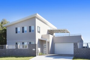 Two-story residential building with a flat roof and covered garage entrance, surrounded by a low wall.