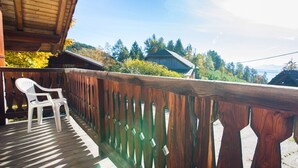 A wooden deck with a white chair, a wooden railing, and a view of a house and trees in the background. - Vacation Apartment "Malgorerhof Mathilde" with Mountain View, Wi-Fi and Balcony (Jenesien)