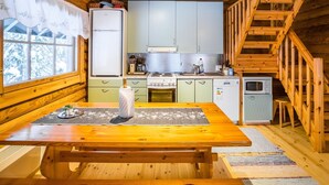 Ein gemütliches Blockhaus-Interieur mit einem Holzesstisch, einer Küche mit hellgrünen Schränken, einem kleinen Kühlschrank und einer Holztreppe.