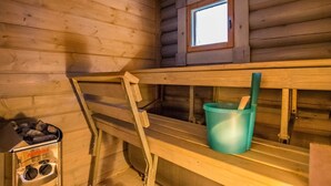 Ein Holzblockhaus-Innenraum mit Etagenbett, kleinem Fenster, Heizung und Eimer.