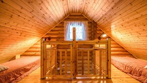 Ein gemütliches Schlafzimmer im Dachgeschoss mit Holzbalkendecke, einem Fenster mit Vorhängen und zwei Einzelbetten.