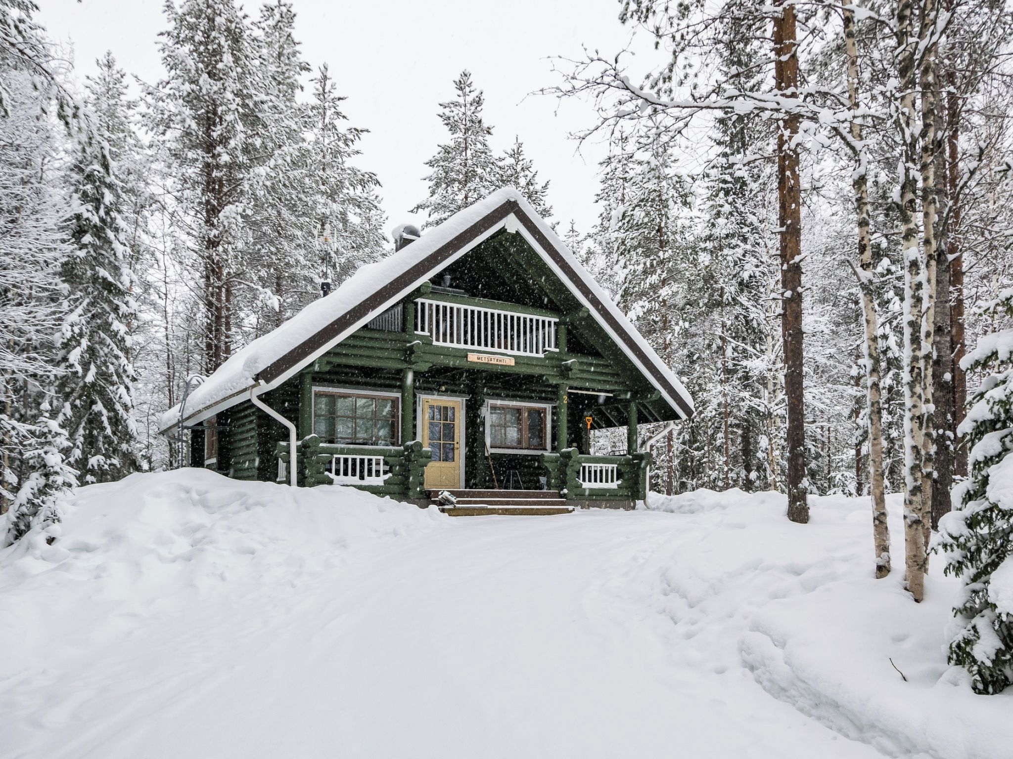 A log cabin with a front porch, surrounded by snow-covered trees.