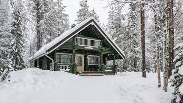 A log cabin with a front porch, surrounded by snow-covered trees.
