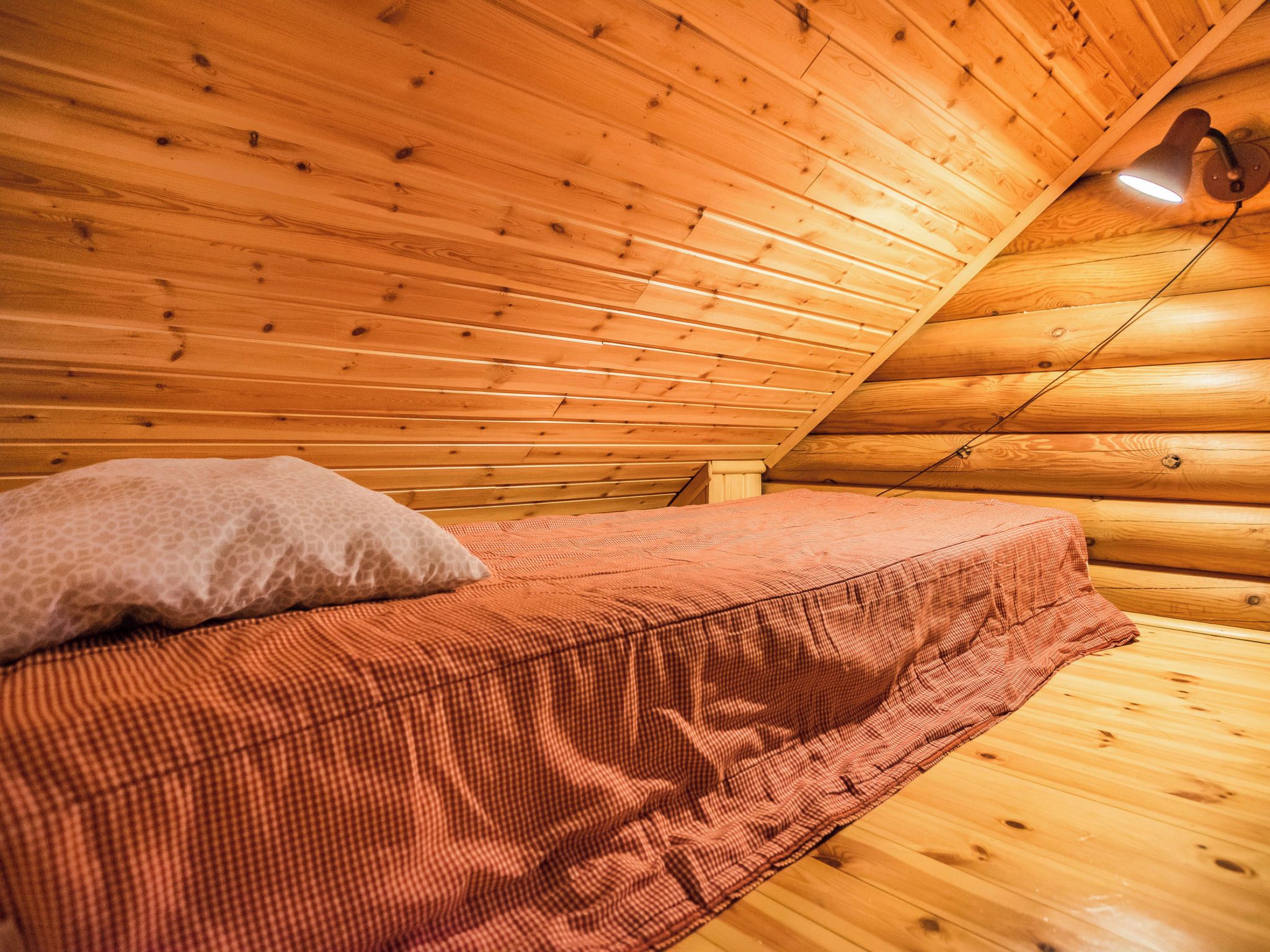 L’intérieur d’une cabane en bois, avec un lit, un oreiller et un plafond en pente.